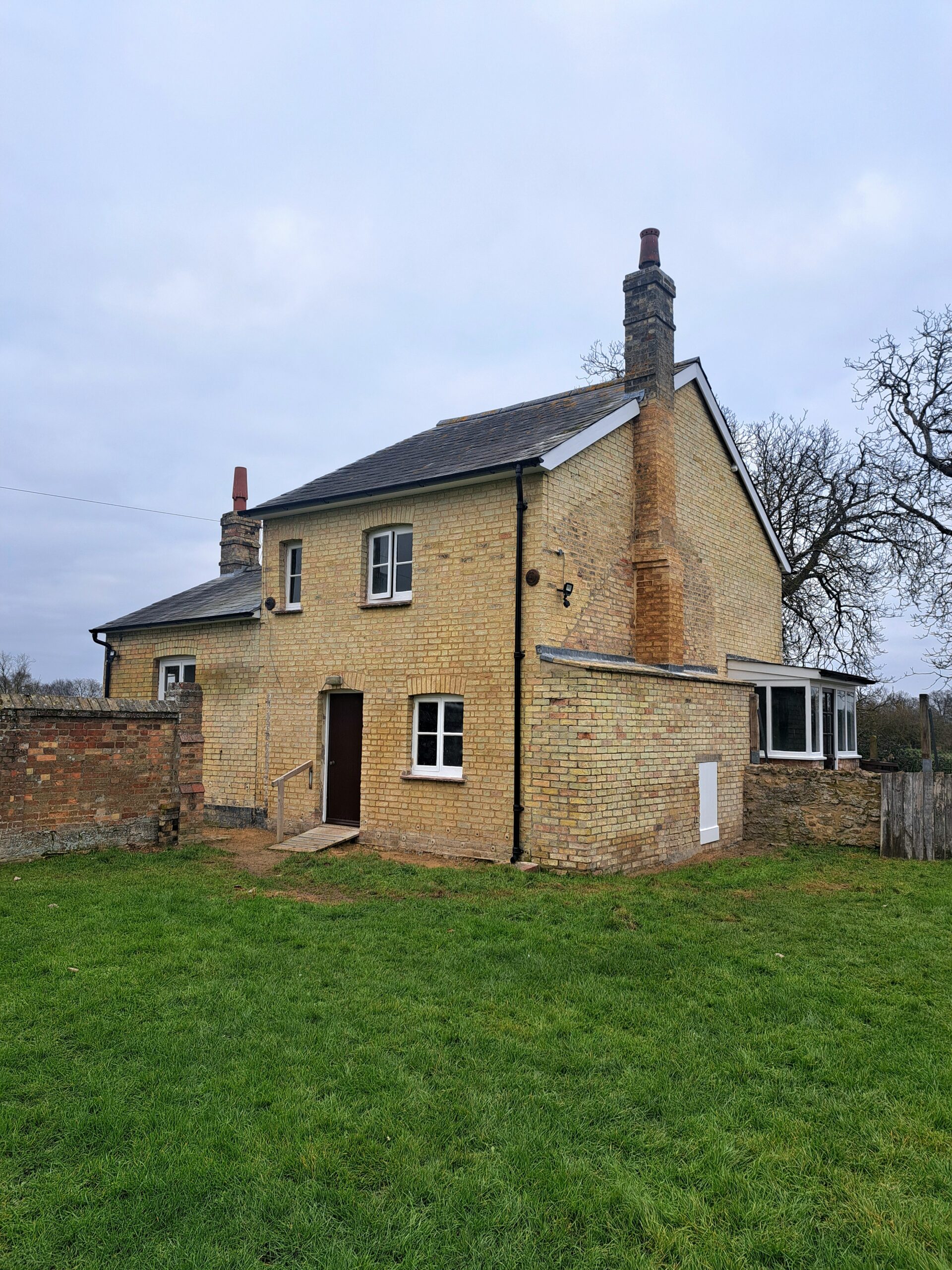 External view of a cottage with a chimney. A black front door and 3 windows.