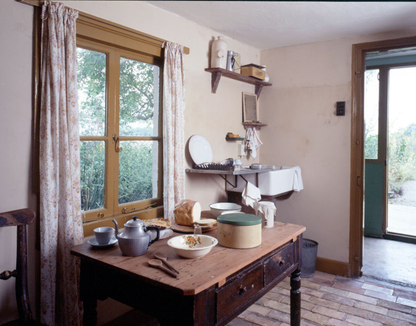 Internal view of a 1940s kitchen with baking implements on a table by a window.