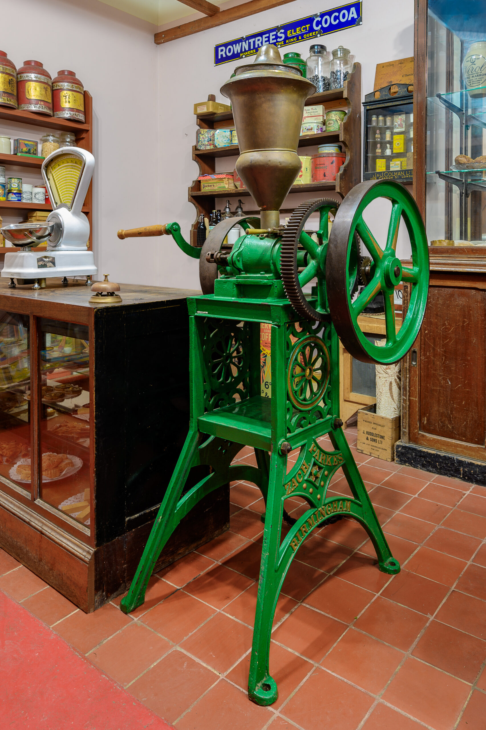 A green metal coffee mill with two big cogs and handle for turning.