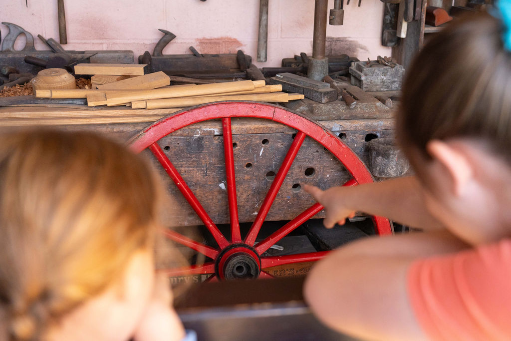 Two girls looking at a large red, wooden wheel.