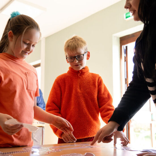 Two children assembling a paper skeleton on a table with a member of the Education Team.