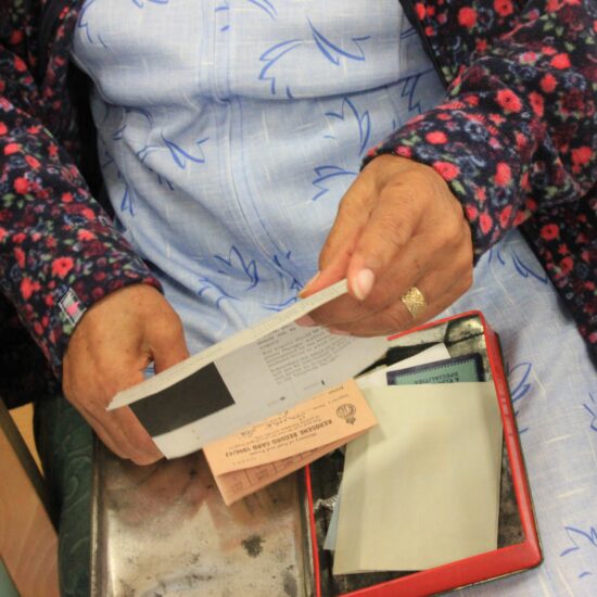 A box of documents in the lap of an elderly woman. She is holding one of the documents in their hands.