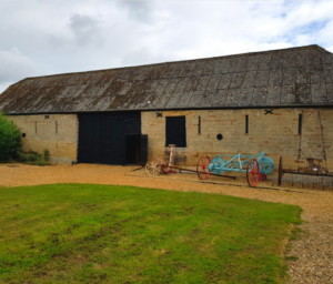 A stone barn with black wooden large doors sitting in front of a patch of grass. 