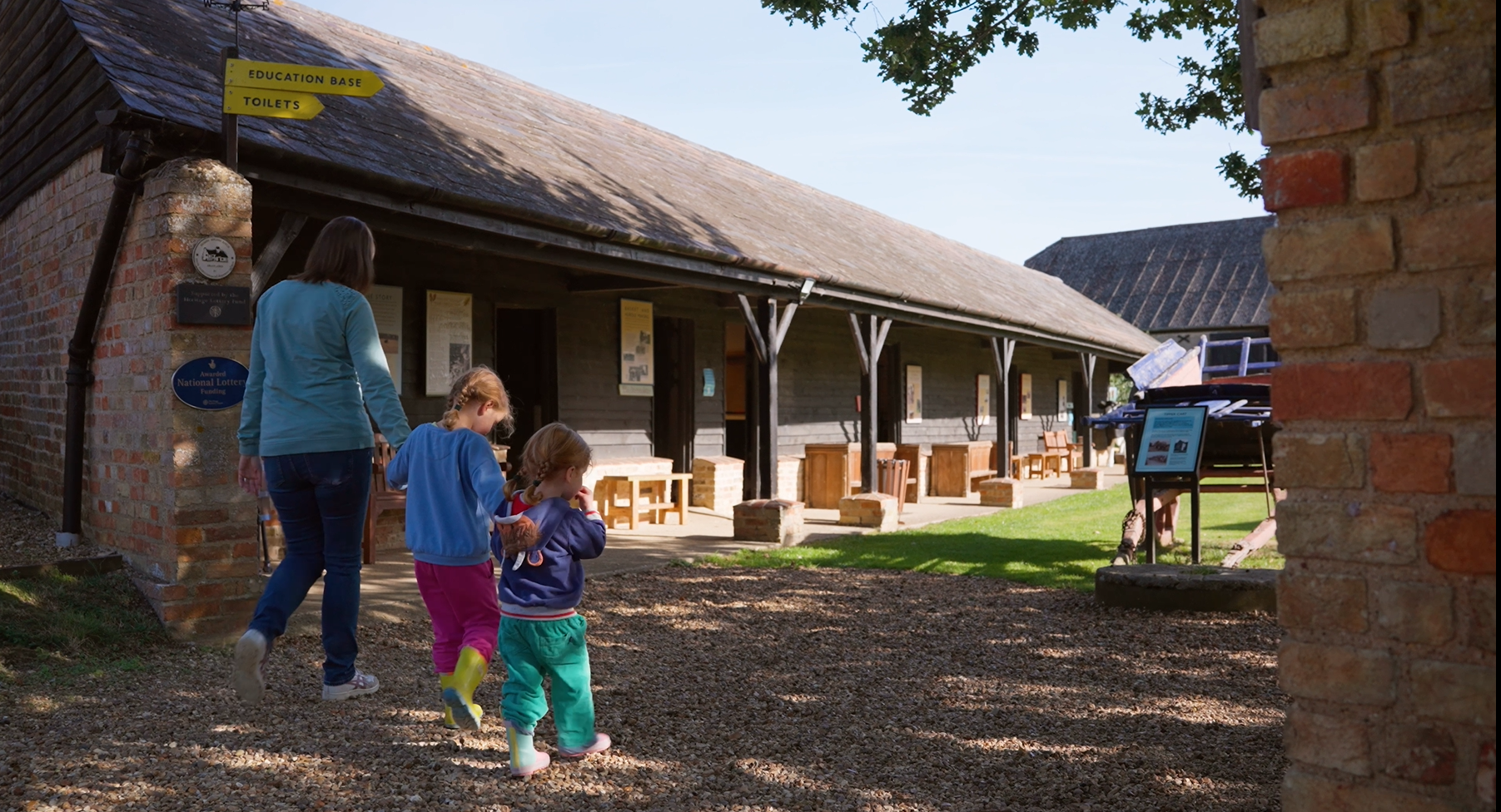 Woman and two children walking beside farm buildings that would have housed pigs