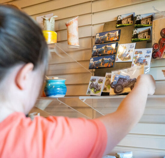 Girl taking a tractor magnet off a shelf in museum gift shop.